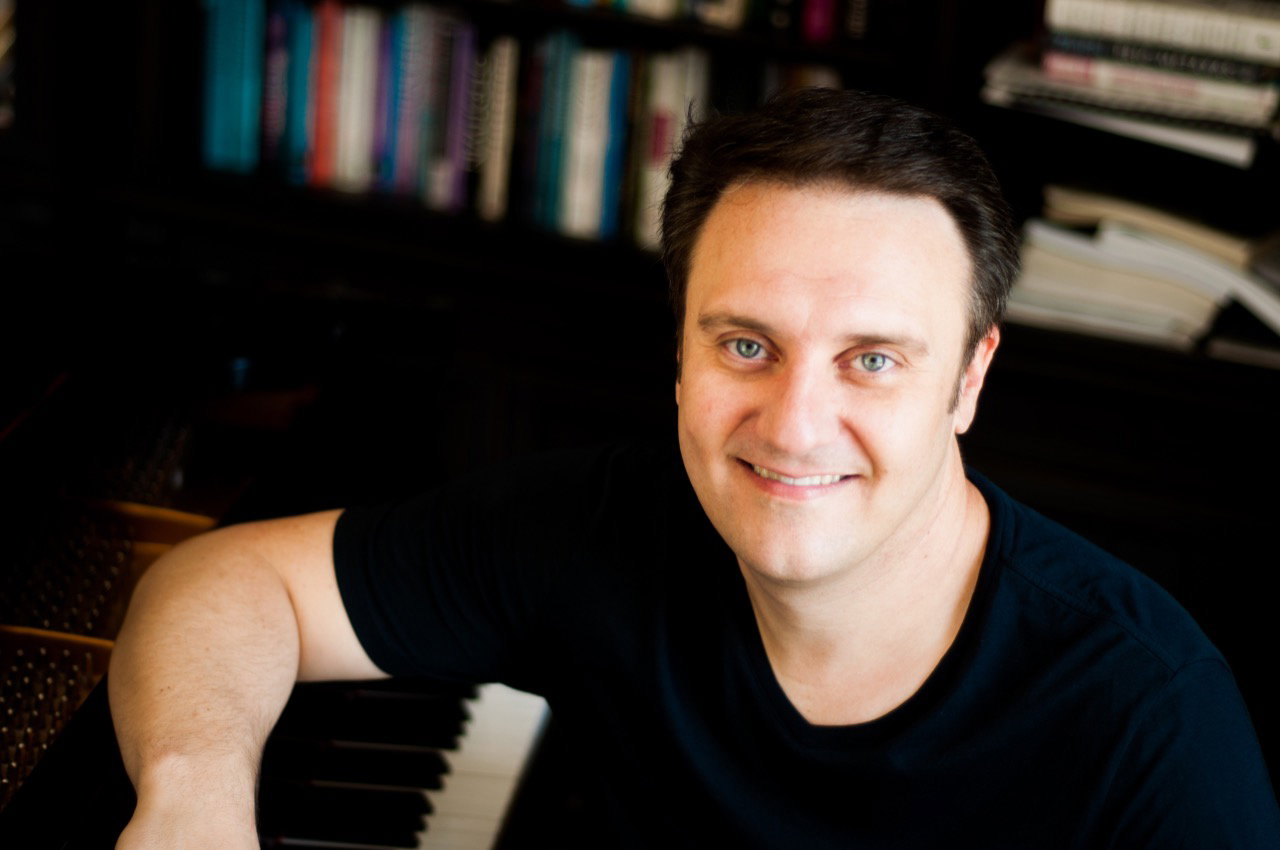 Jason Webb smiling at the piano in front of bookshelves