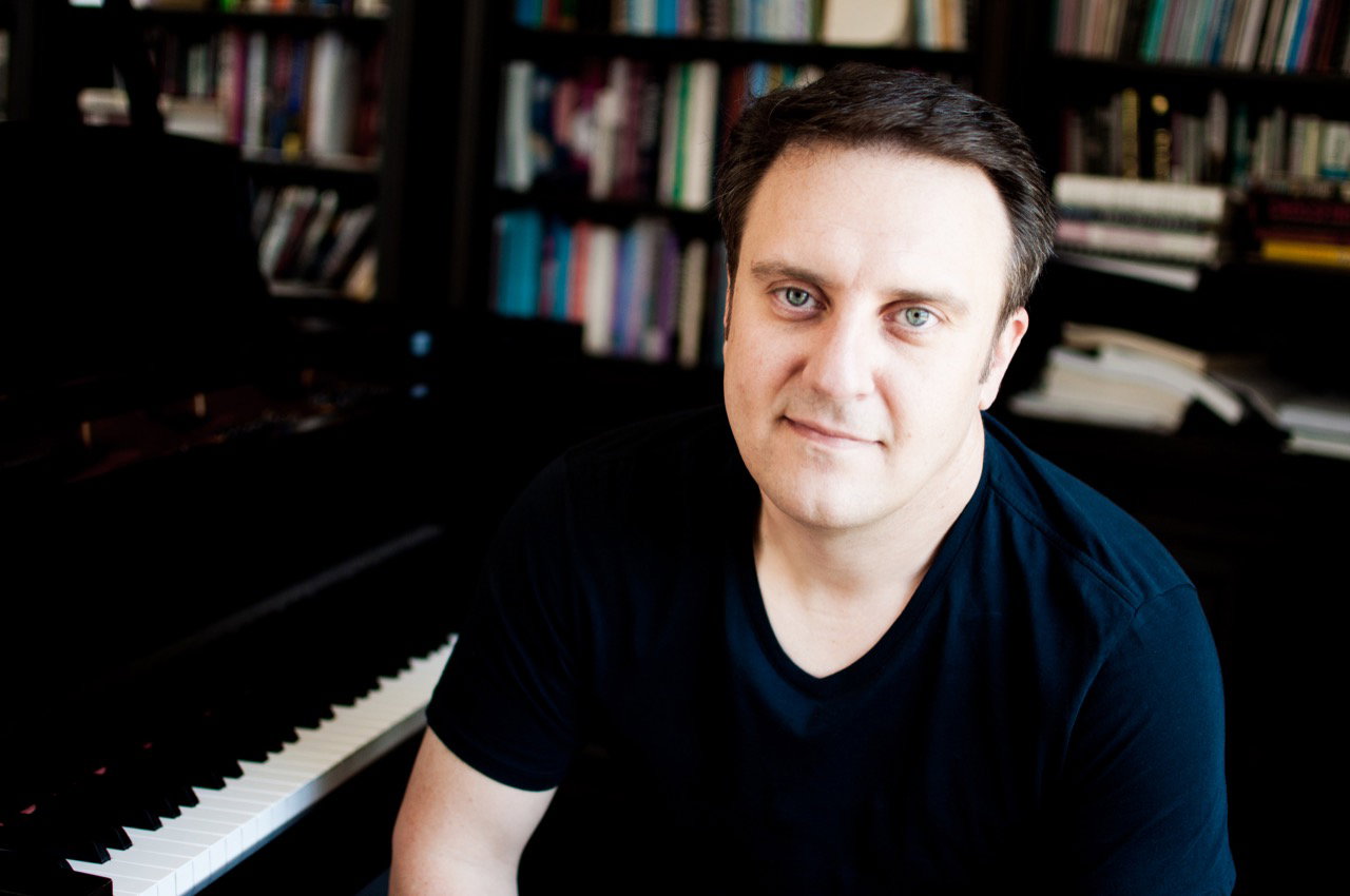 Jason Webb seated at the piano in front of bookshelves