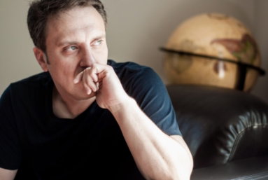 Jason Webb resting his chin on his hand beside a globe