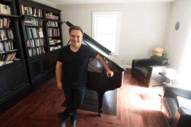 Jason Webb standing beside a grand piano in his music room